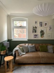 Interior view of a cosy living room featuring a Residence Collection window with grid-style panes, allowing natural light to fill the space. The room is decorated with a comfortable leather sofa, throw pillows, and wall art, creating a warm and inviting atmosphere