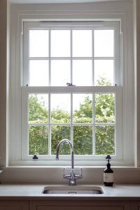 White uPVC sliding sash window above a kitchen sink, overlooking a green garden.